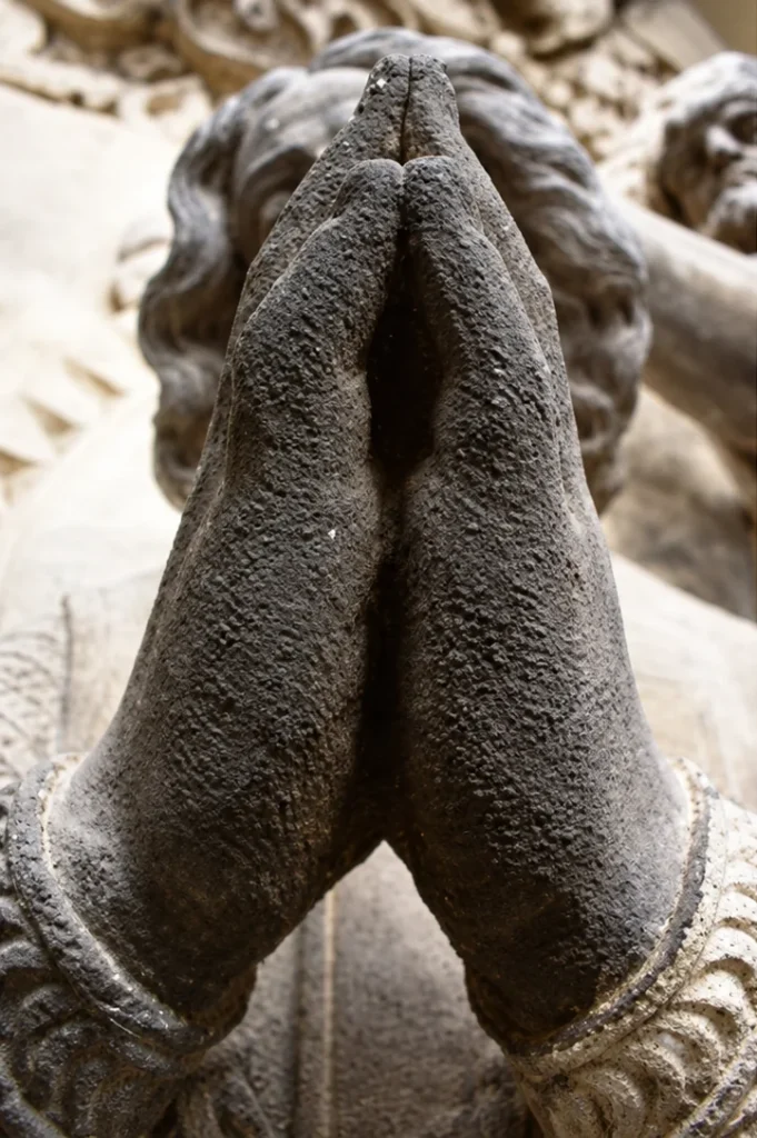 Mains jointes d’une sculpture en pierre couvertes d’un encrassement gris foncé, avant nettoyage laser