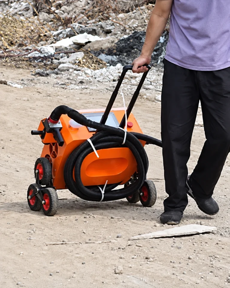 Un opérateur tire le décapeur laser 500 W PRO par sa poignée télescopique sur un chemin de terre et de gravats